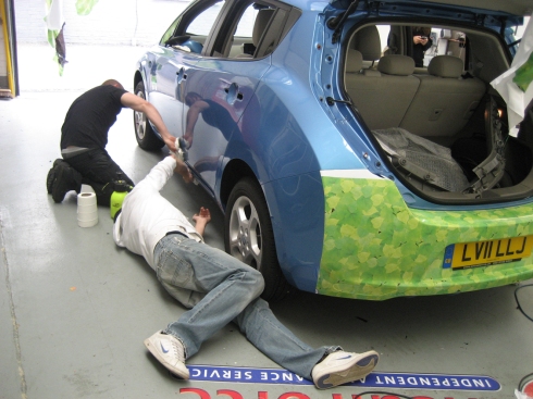 Workers lying down on the ground cleaning the lowers sections of the Nissan Leaf